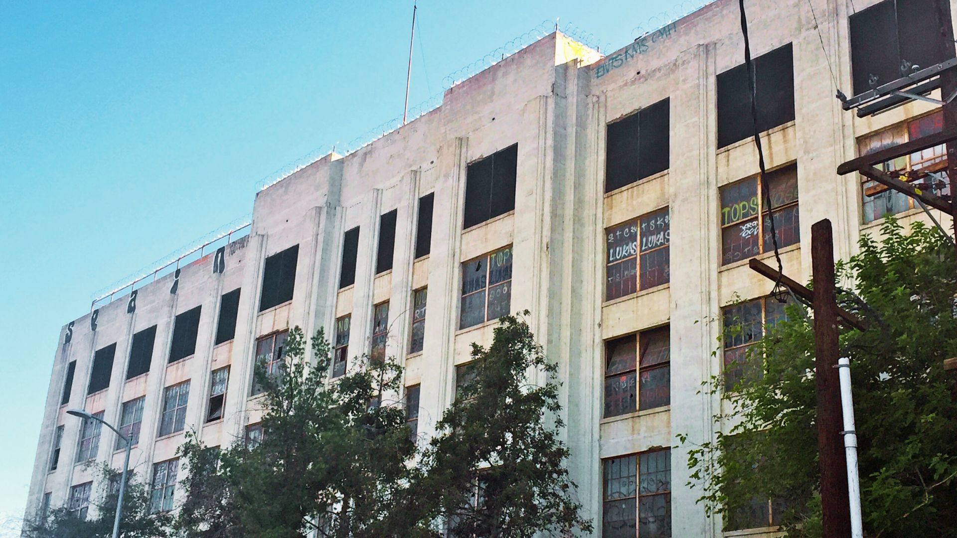 Weathered industrial building with broken windows, graffiti, and barbed wire along the roofline.