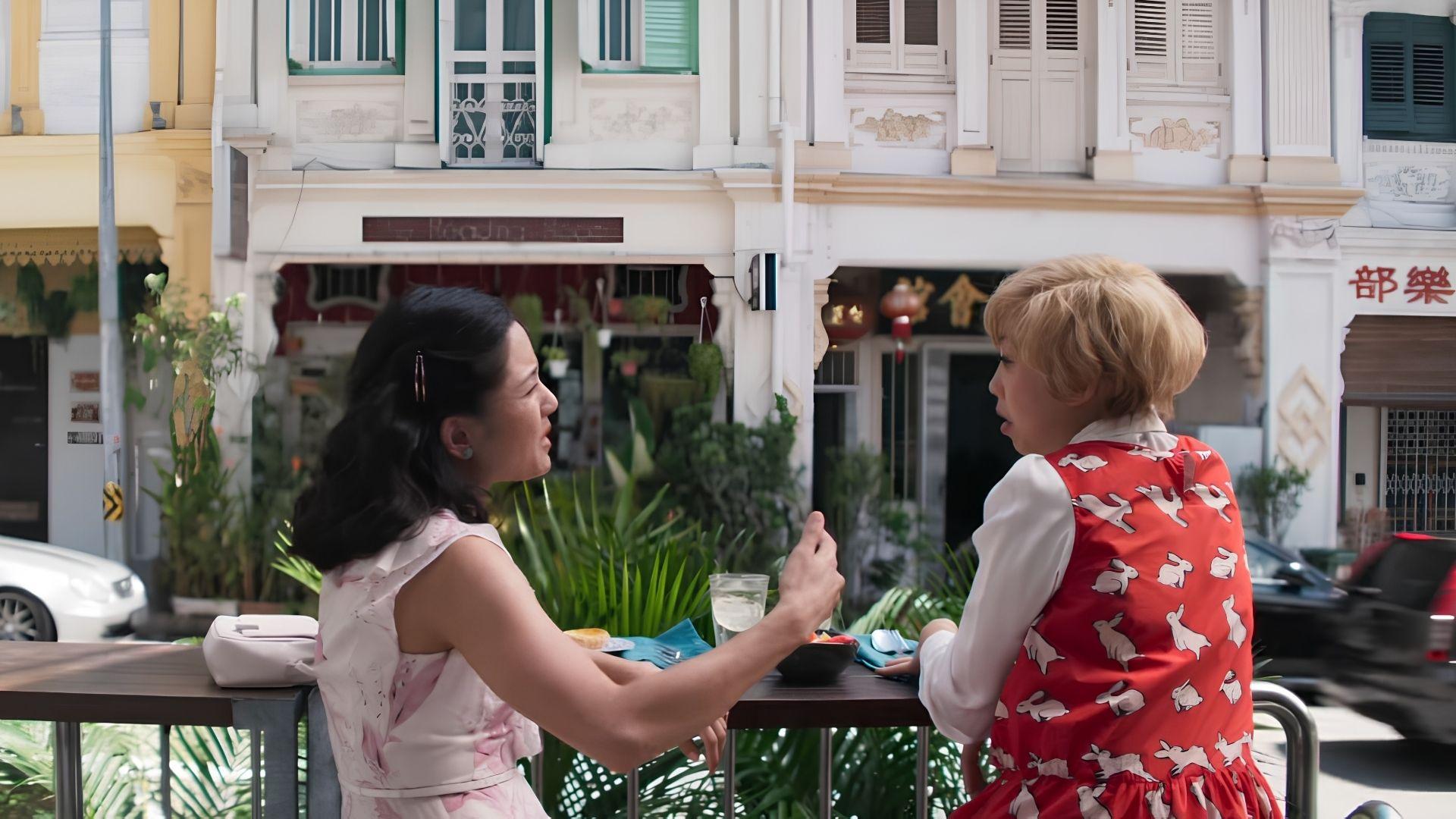 Two women dining at an outdoor table in front of Peranakan shophouses in Chinatown.