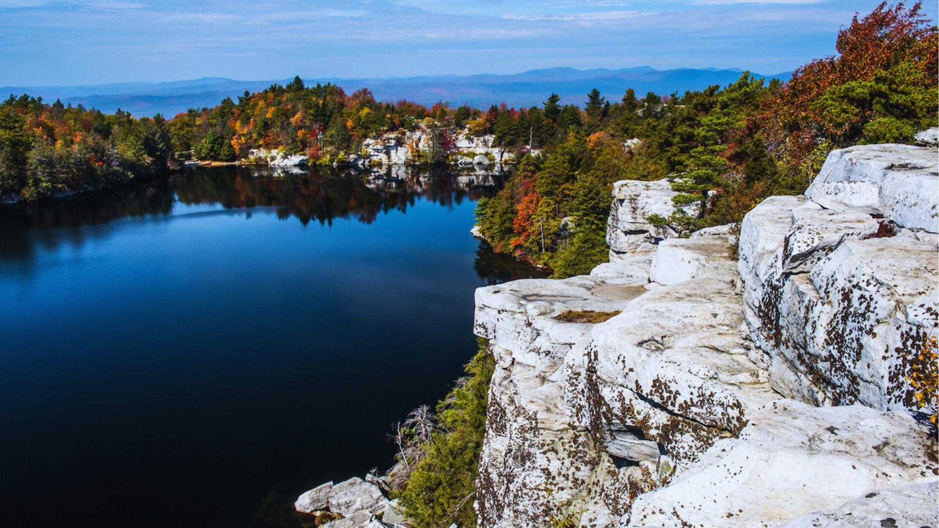 Aerial view of Lake Minnewaska surrounded by white cliffs and fall foliage, featured in hiking scenes in Severance.