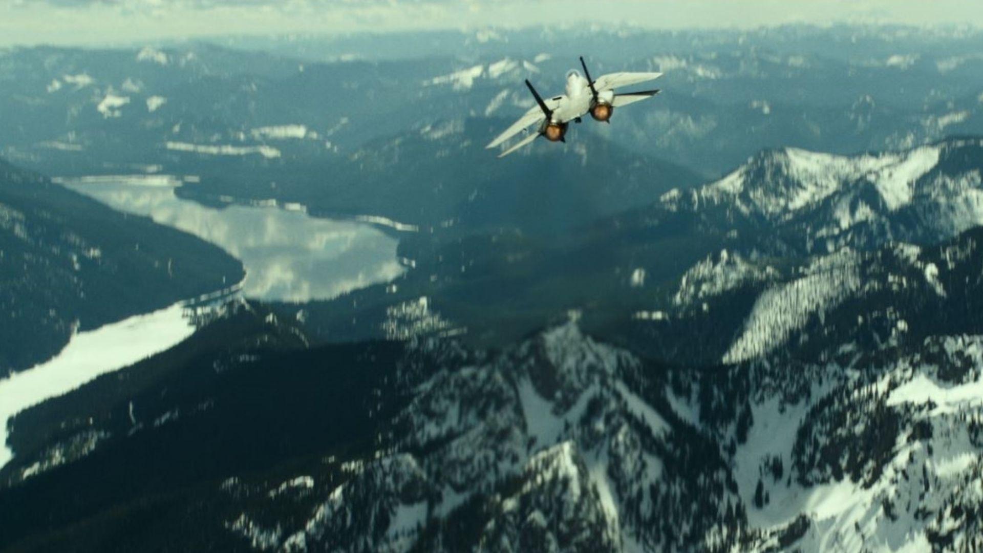 op Gun: Maverick. F-14 Tomcat climbs steeply over snow-covered mountains and a frozen lake below.