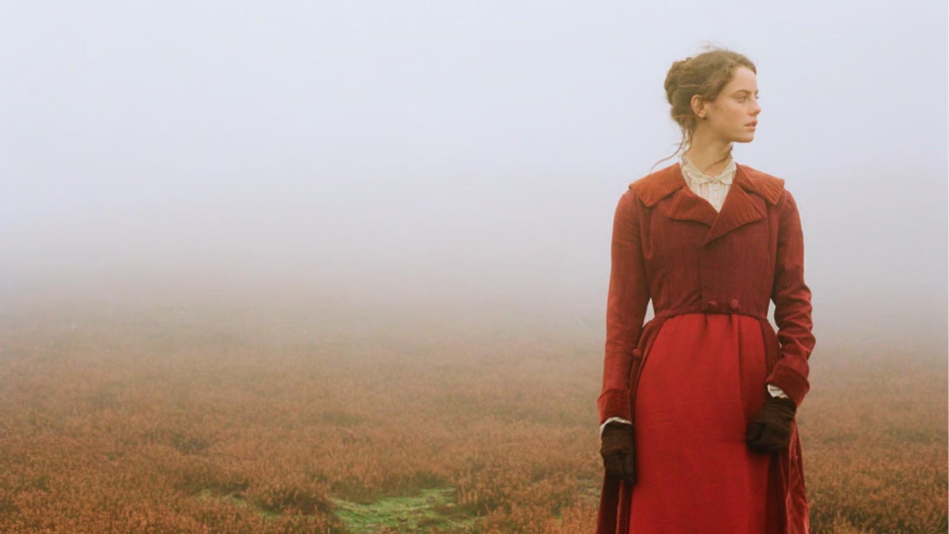 Woman in red Victorian coat standing alone on misty Yorkshire moors, Wuthering Heights filming location.