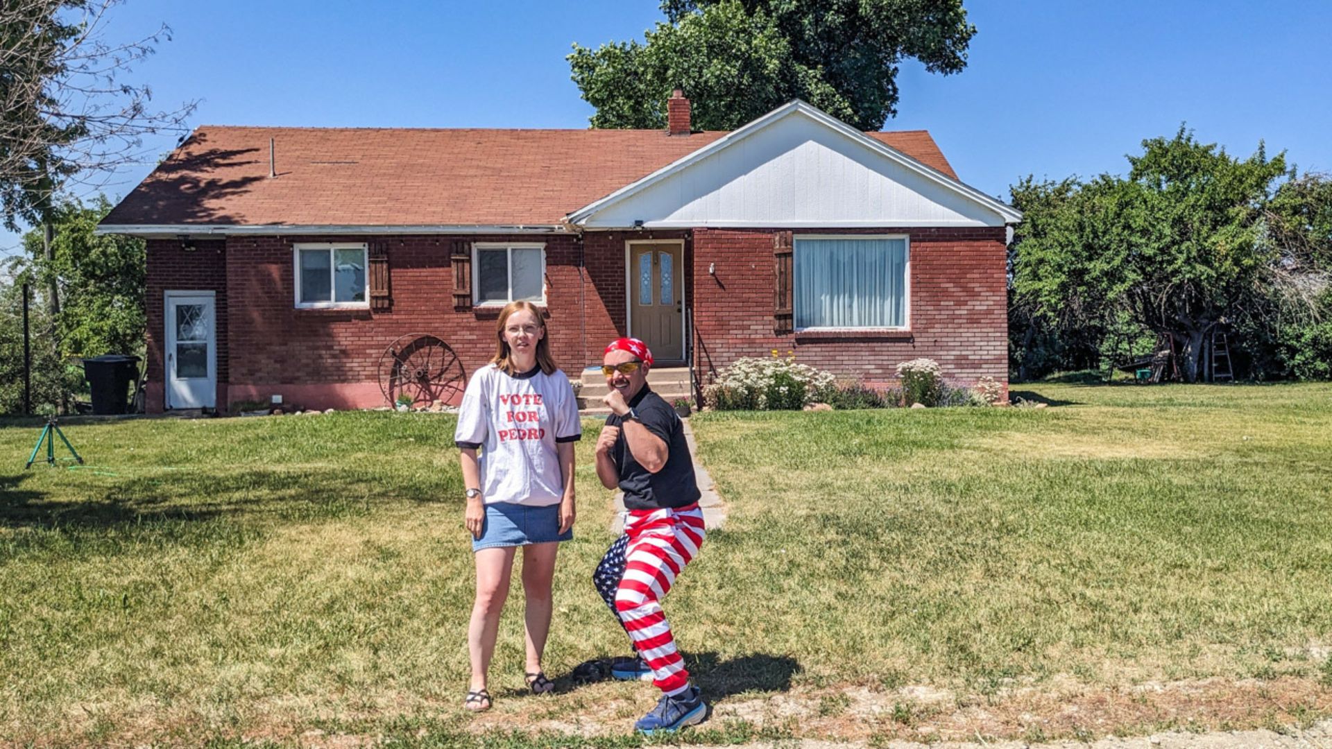 A couple dressed in patriotic clothing stands for a picture in front of a quaint house, showcasing the film's charming locations.