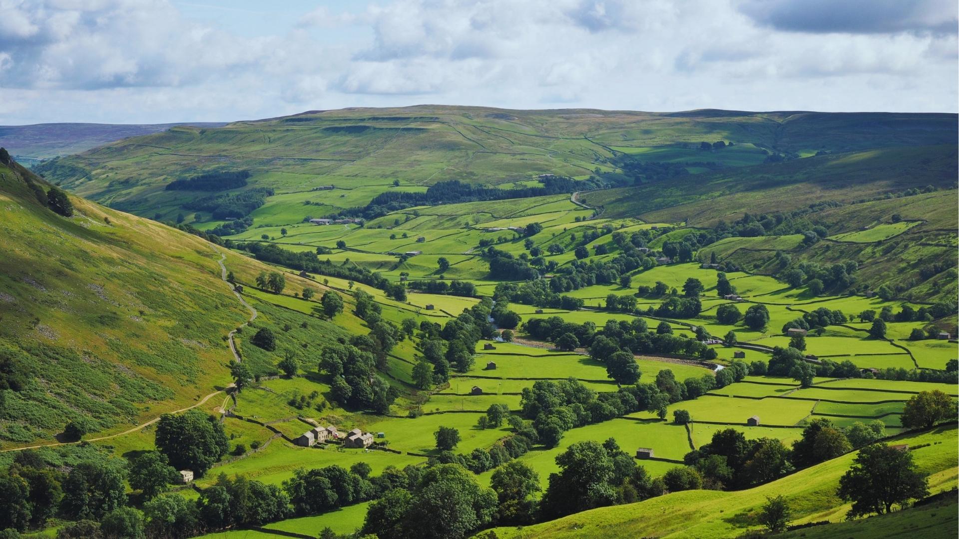 Lush green Yorkshire Dales valley with stone walls and farms, moorland filming location for Wuthering Heights.