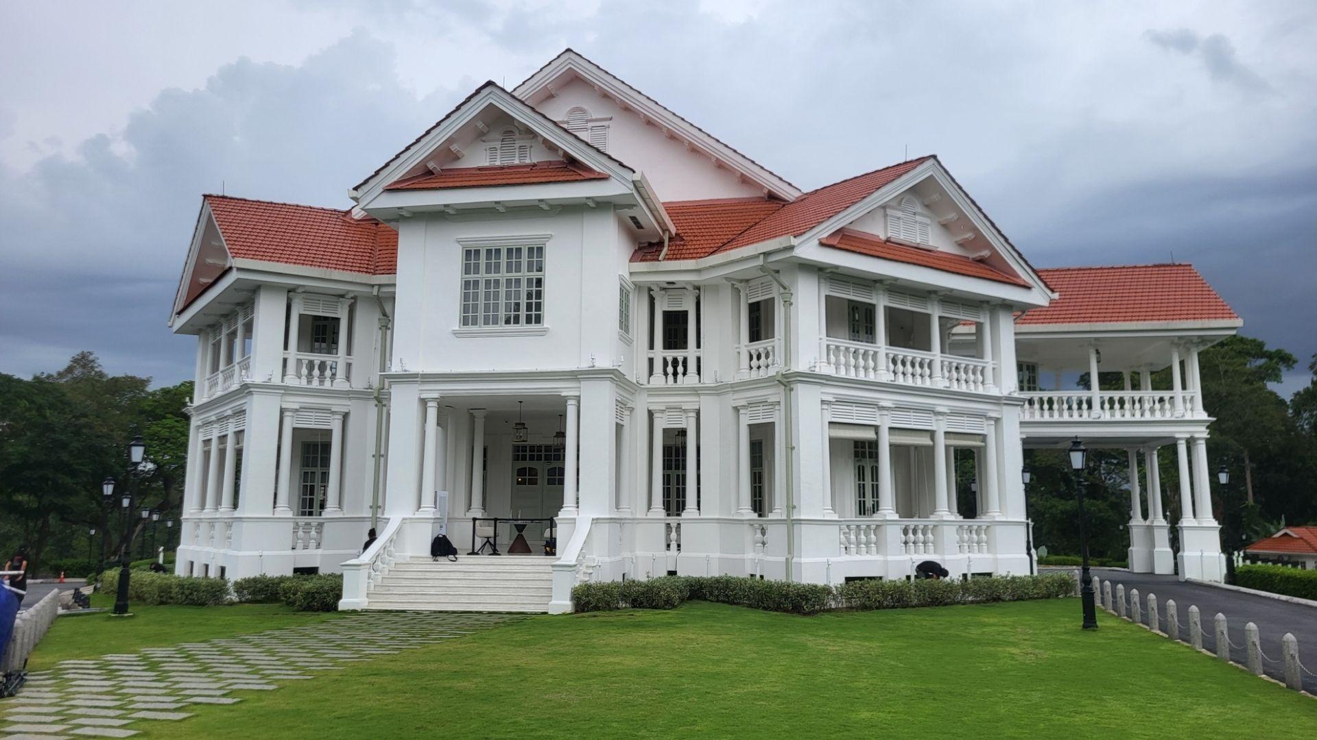 A grand white colonial mansion with a red-tiled roof and wraparound verandas on a green lawn.