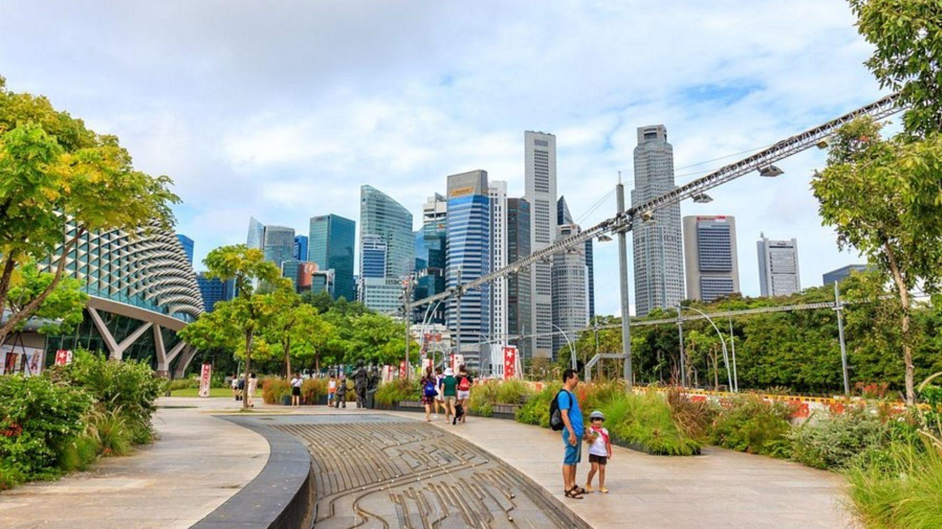 Pedestrians stroll along a tree-lined path near the Singapore skyline and Esplanade