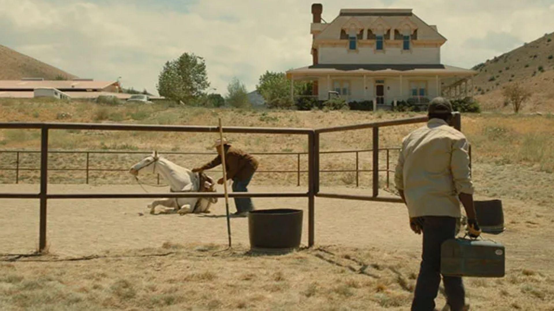 Still from NOPE. OJ watches as a wrangler tends to a fallen white horse in the corral at Haywood Ranch.