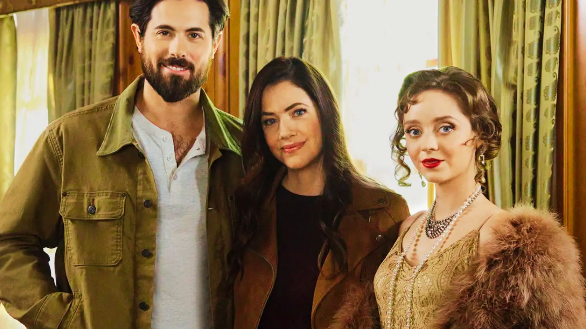 A bearded man in a tan jacket, a woman in a brown jacket, and a 1920s ghost in pearls and fur pose together indoors.