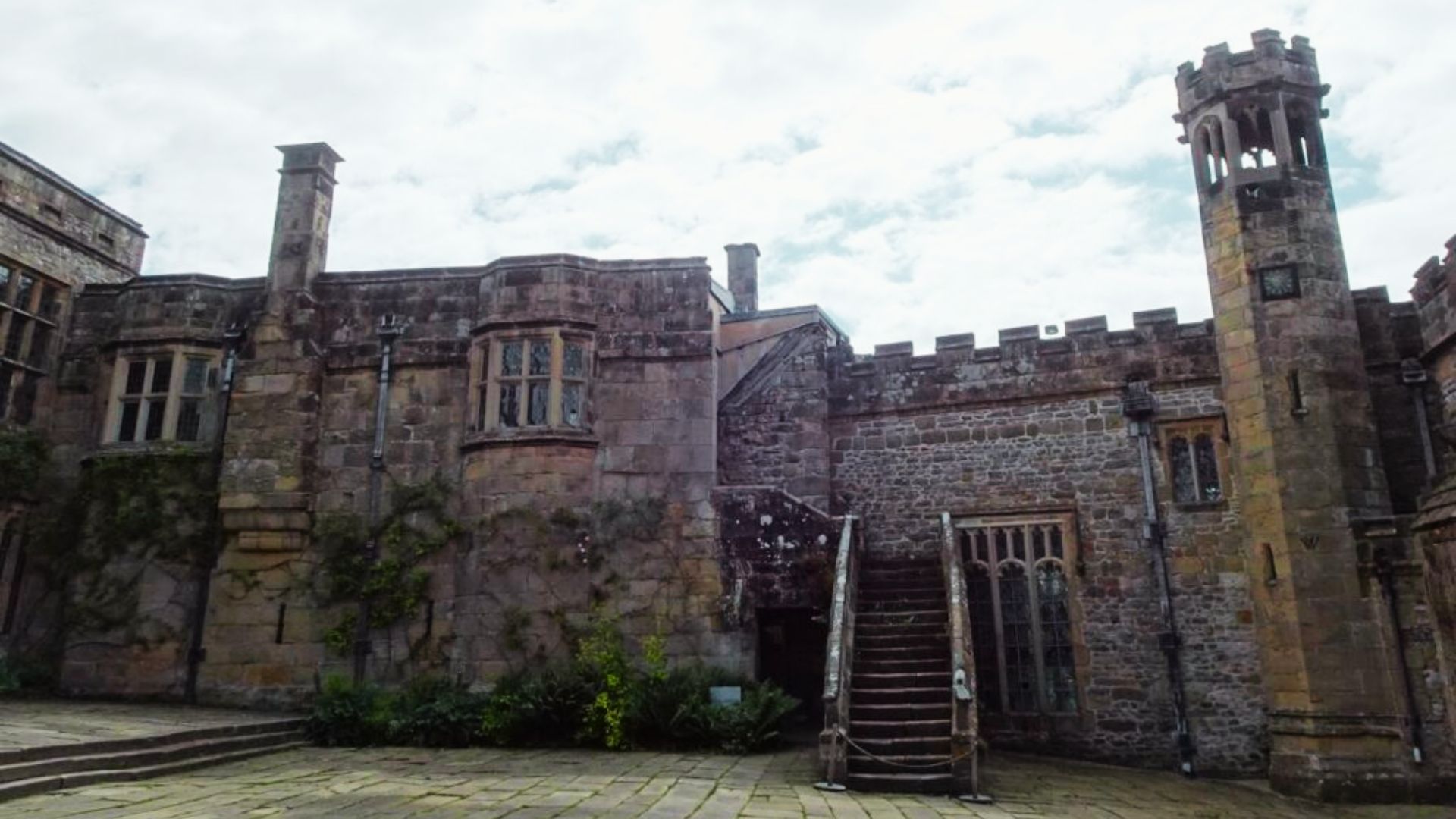 A manicured lawn and stone balustrade frame the ivy-covered facade of Haddon Hall.