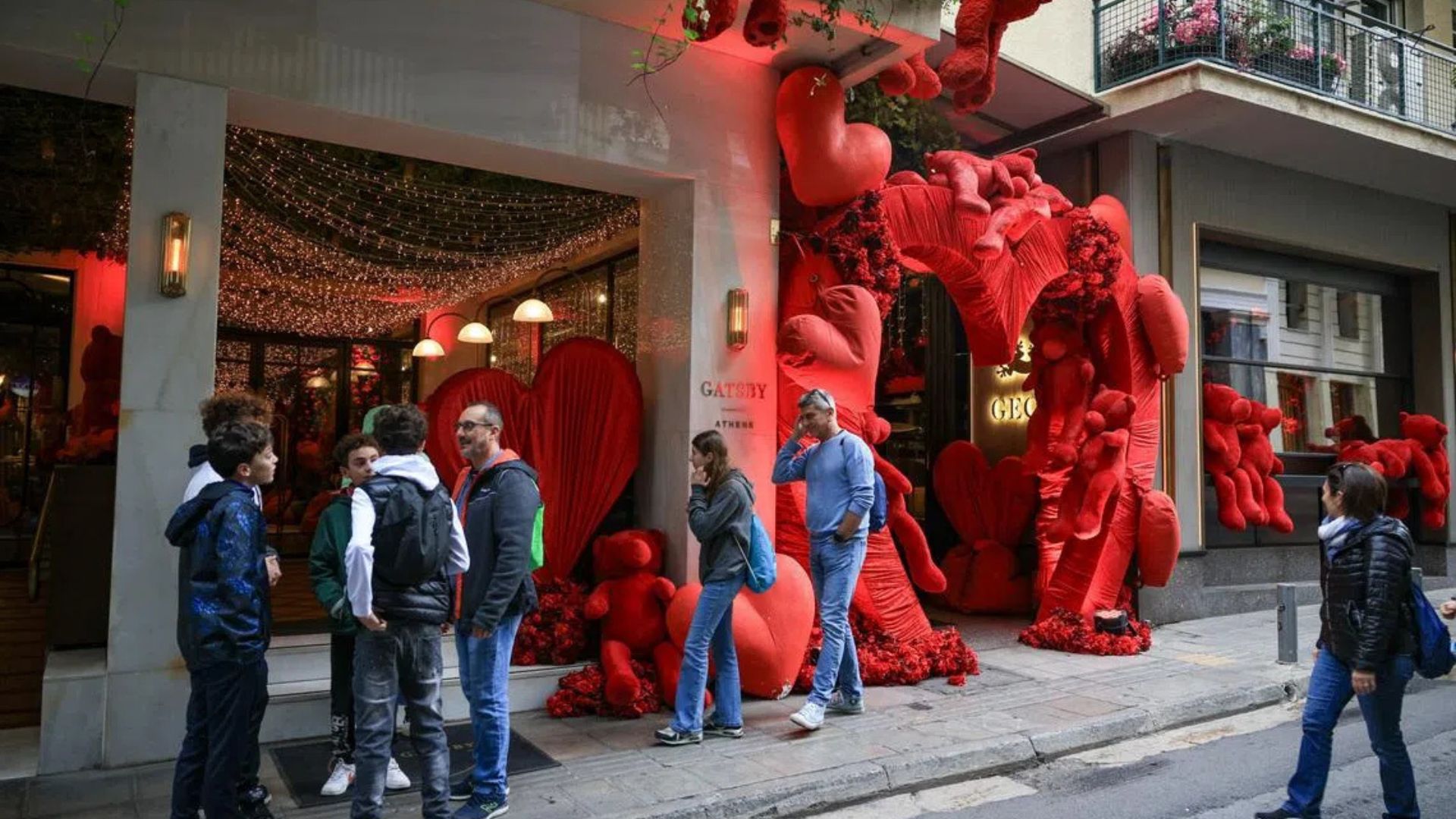 People stroll past a large red heart sculpture on the sidewalk in Athens, Greece, a filming location for the movie Tehran.