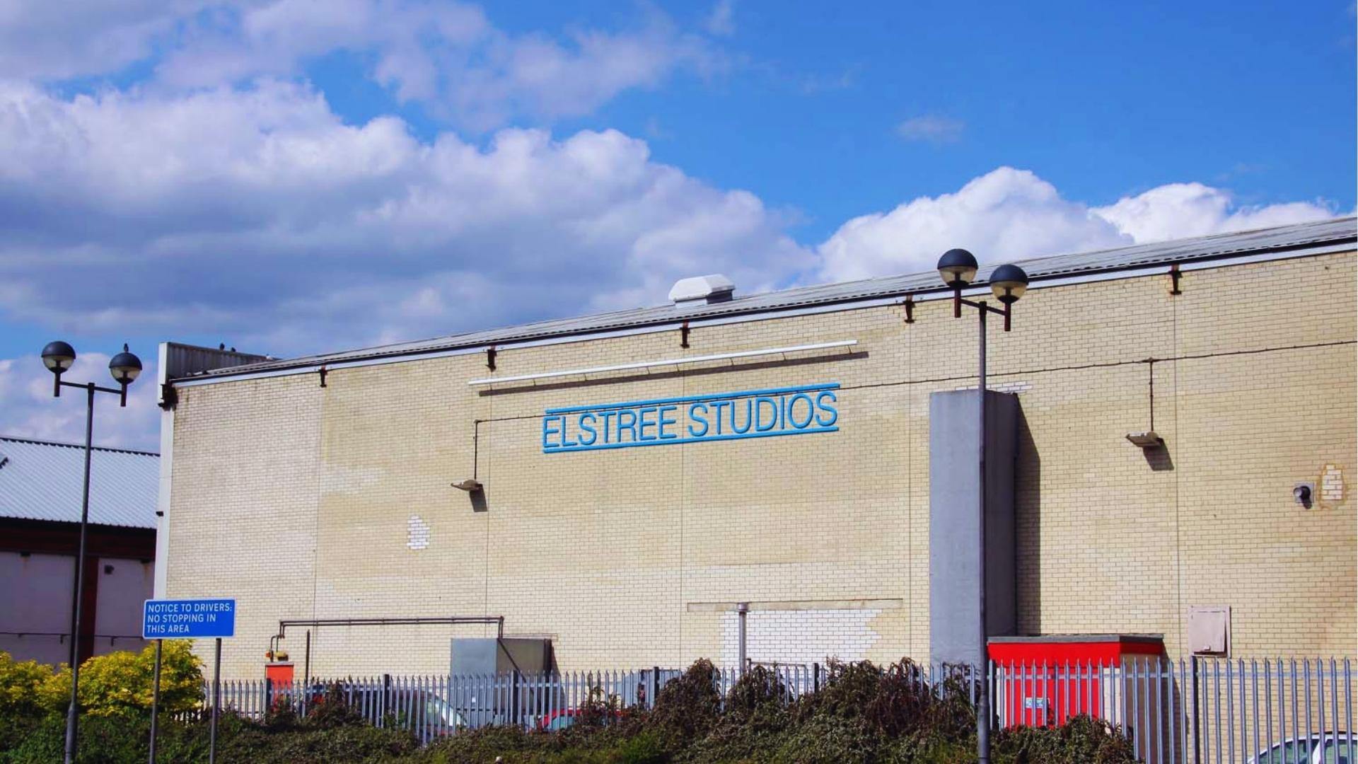 Exterior of Elstree Studios brick building with blue sign, historic UK studio used for Wicked filming.