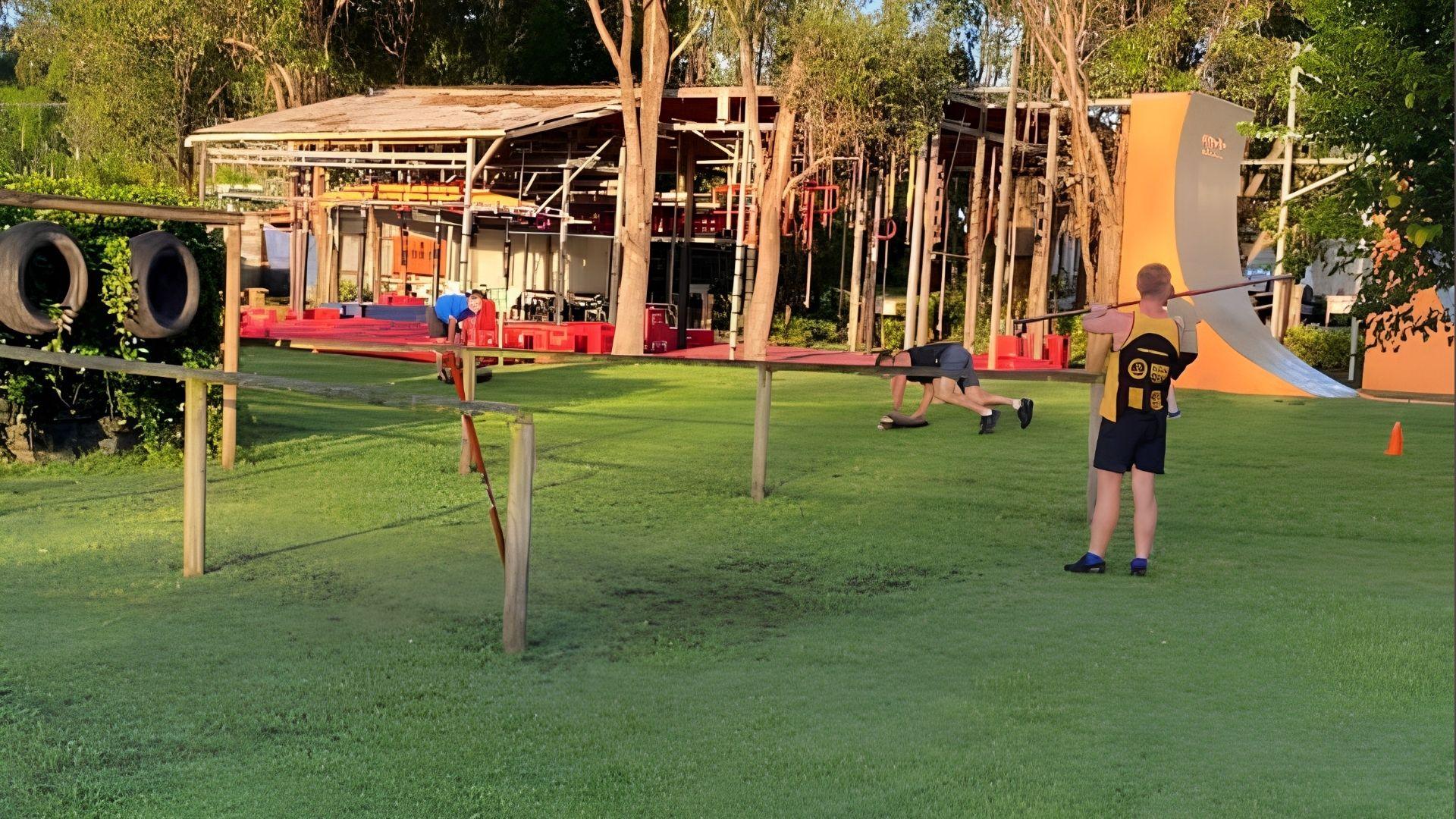 Athletes training at outdoor obstacle course with warped wall and tires on grass