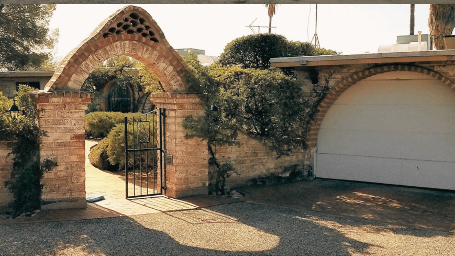Sunlit brick archway and iron gate leading to a courtyard with ivy-covered walls.