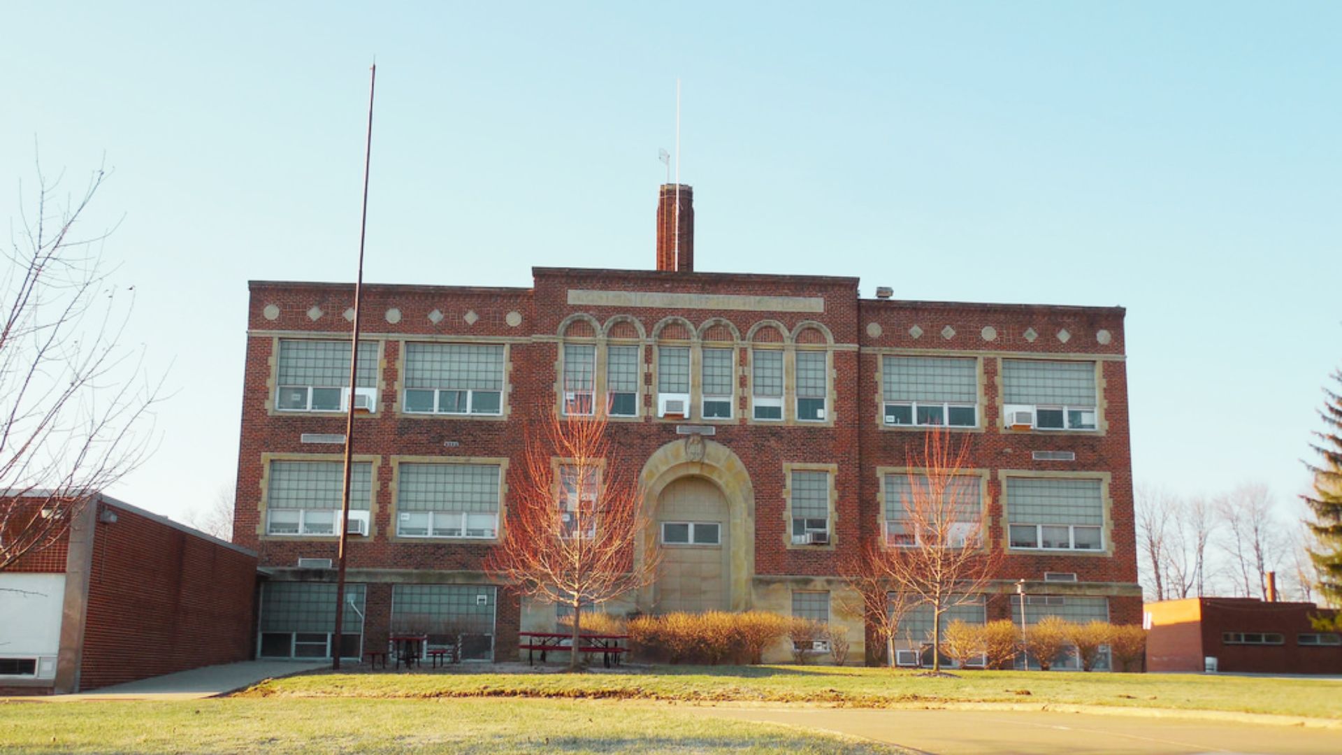 Front view of a three-story brick school building with arched entryway and bare trees.