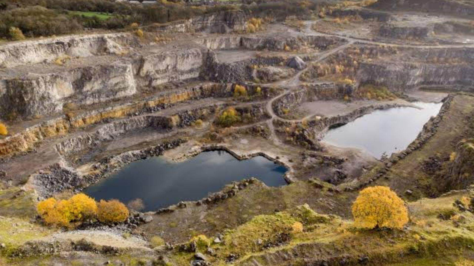 Aerial view of a quarry with tiered rock faces and two flooded pools amid autumn trees.