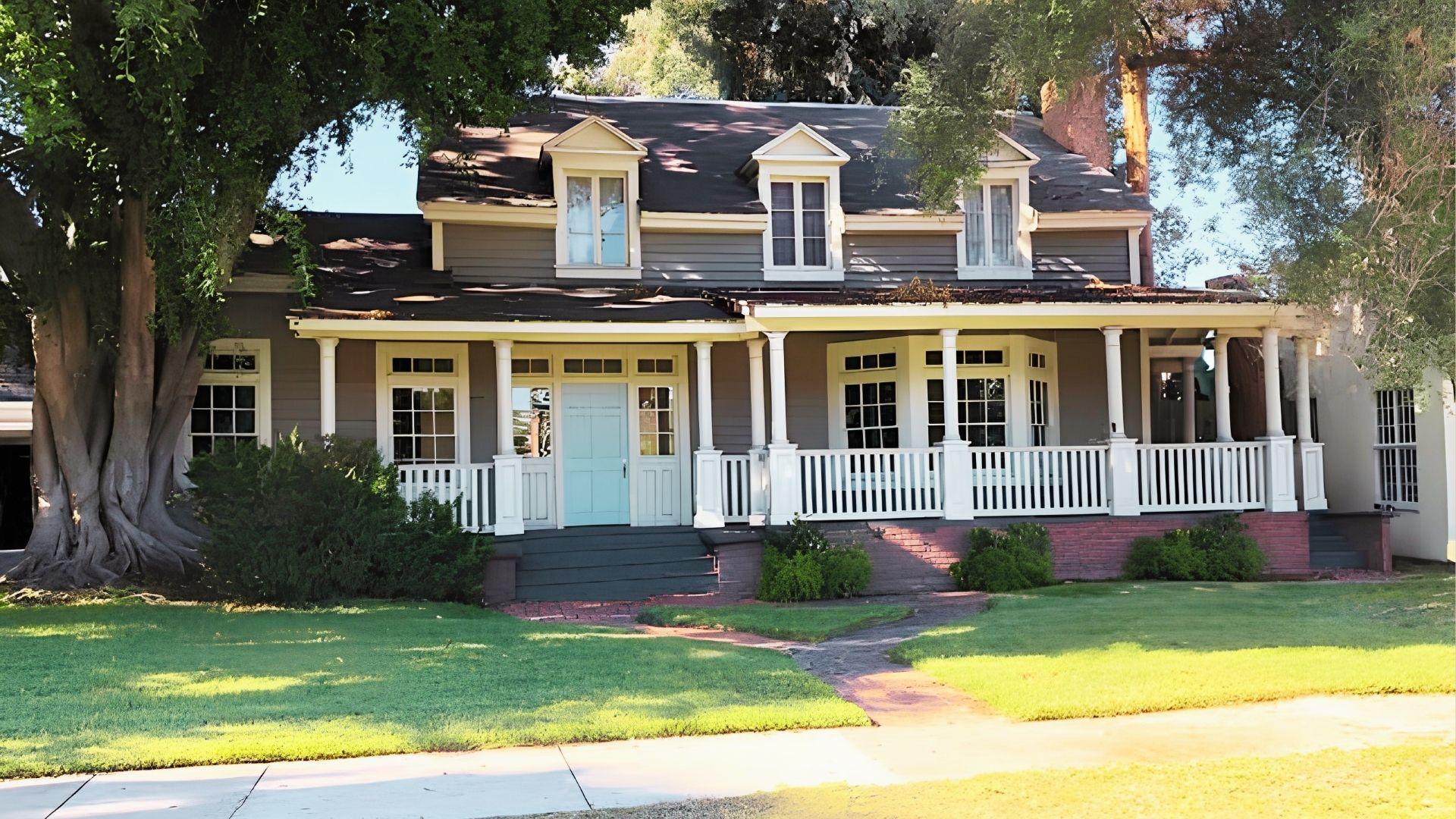 A residential home with an expansive front porch and a towering tree nearby, enhancing the outdoor space.