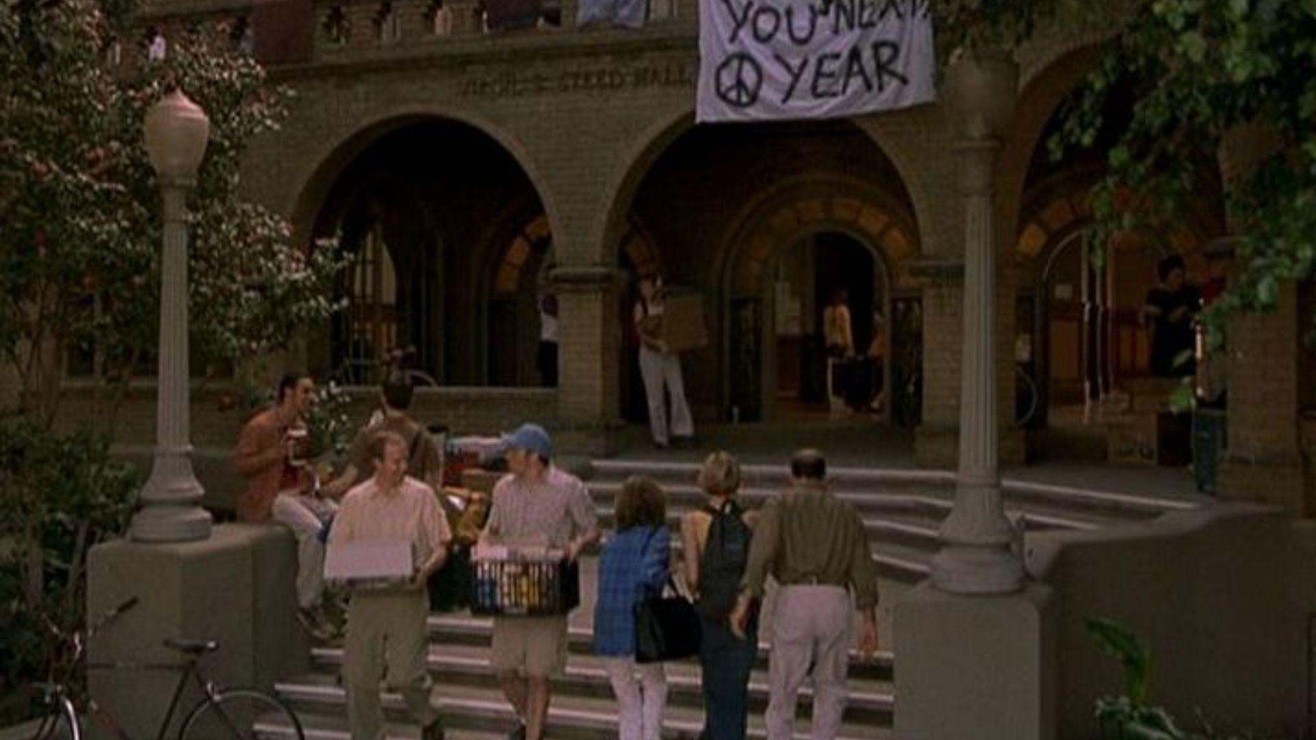 Students on the steps of an arched brick university building with a "See You Next Year" banner.