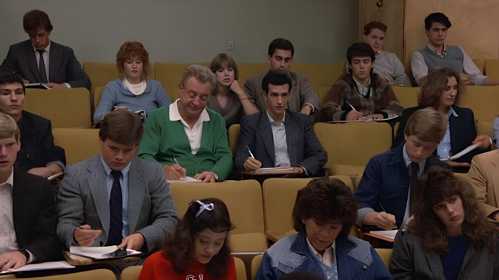 The male lead in a green cardigan sits among students in a university lecture hall.