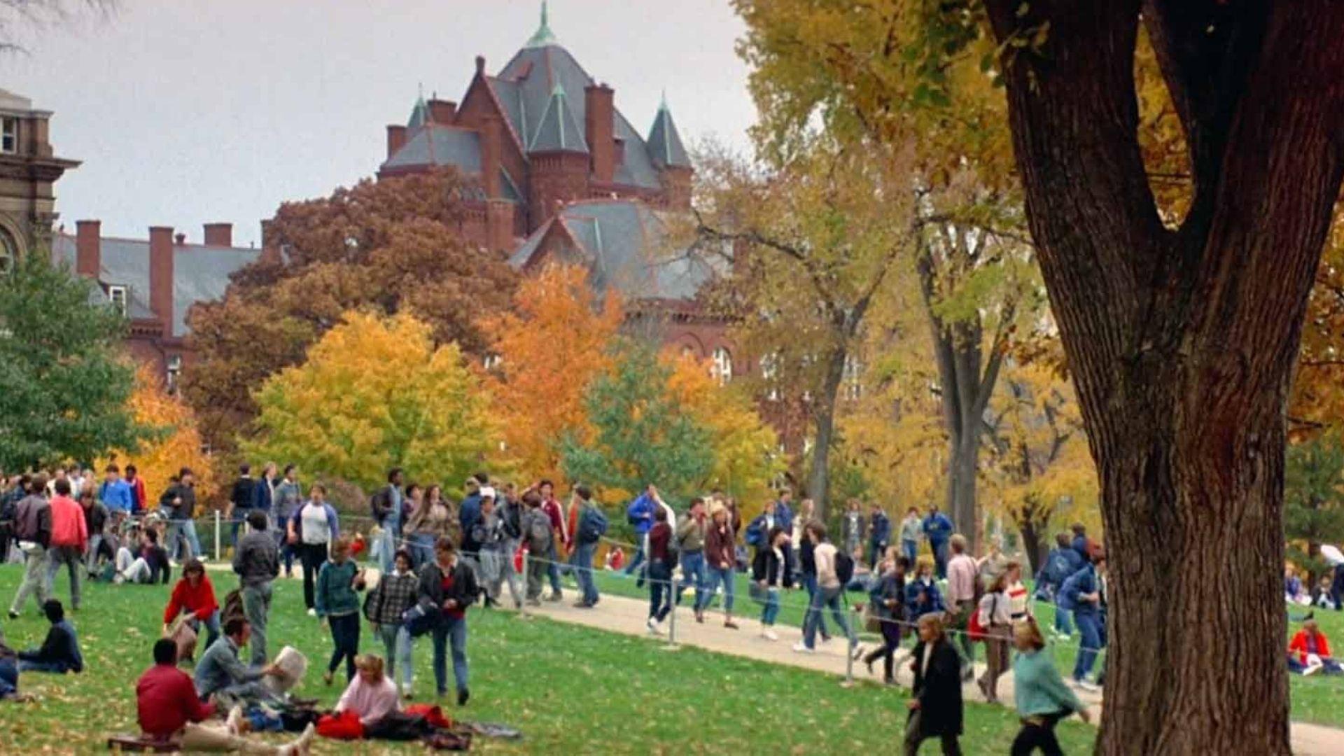 Crowds of students cross a busy campus lawn below Cali State university building in fall.
