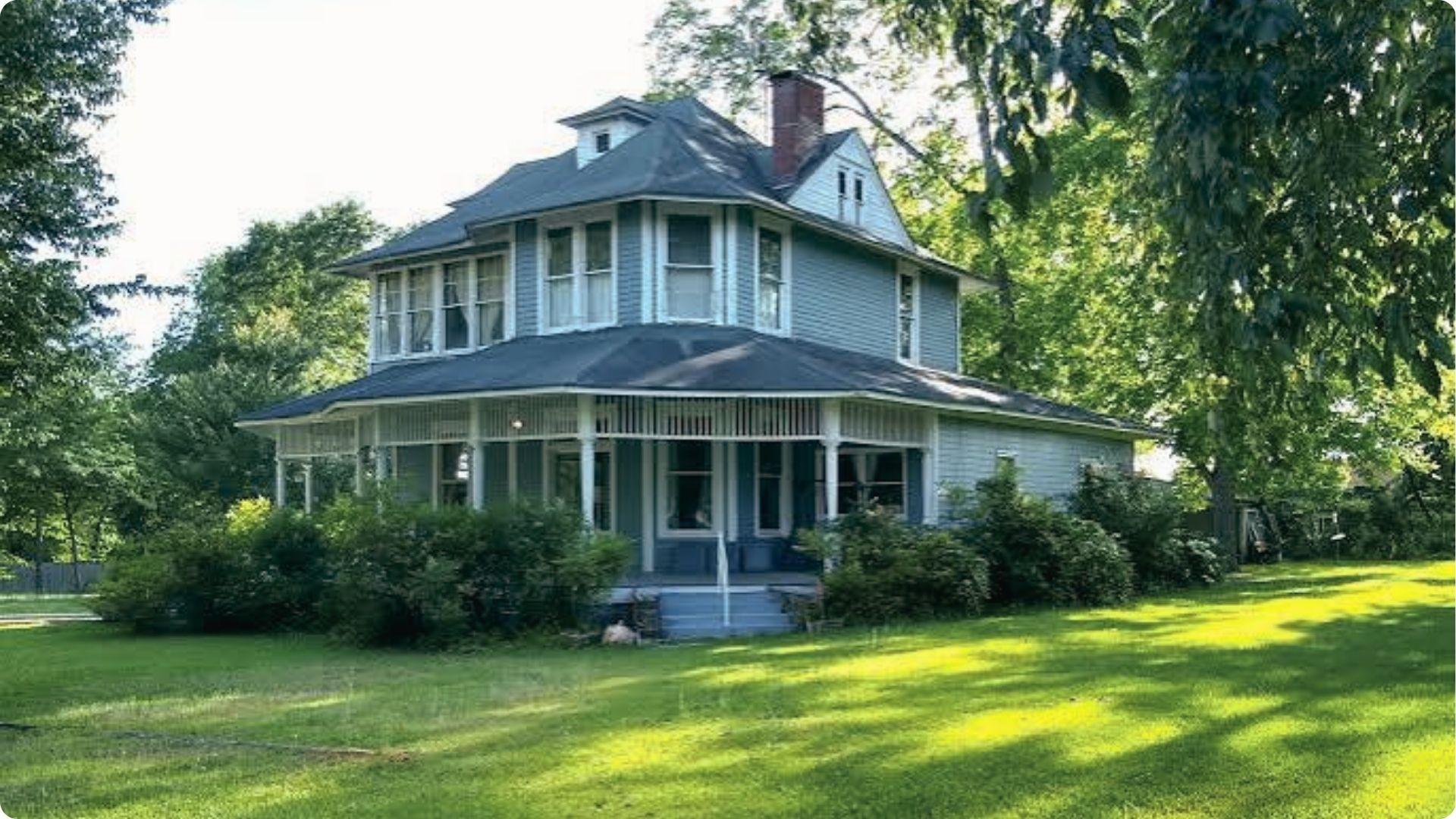 Blue Victorian house with wraparound porch and big lawn, used as Ruth’s house in film.