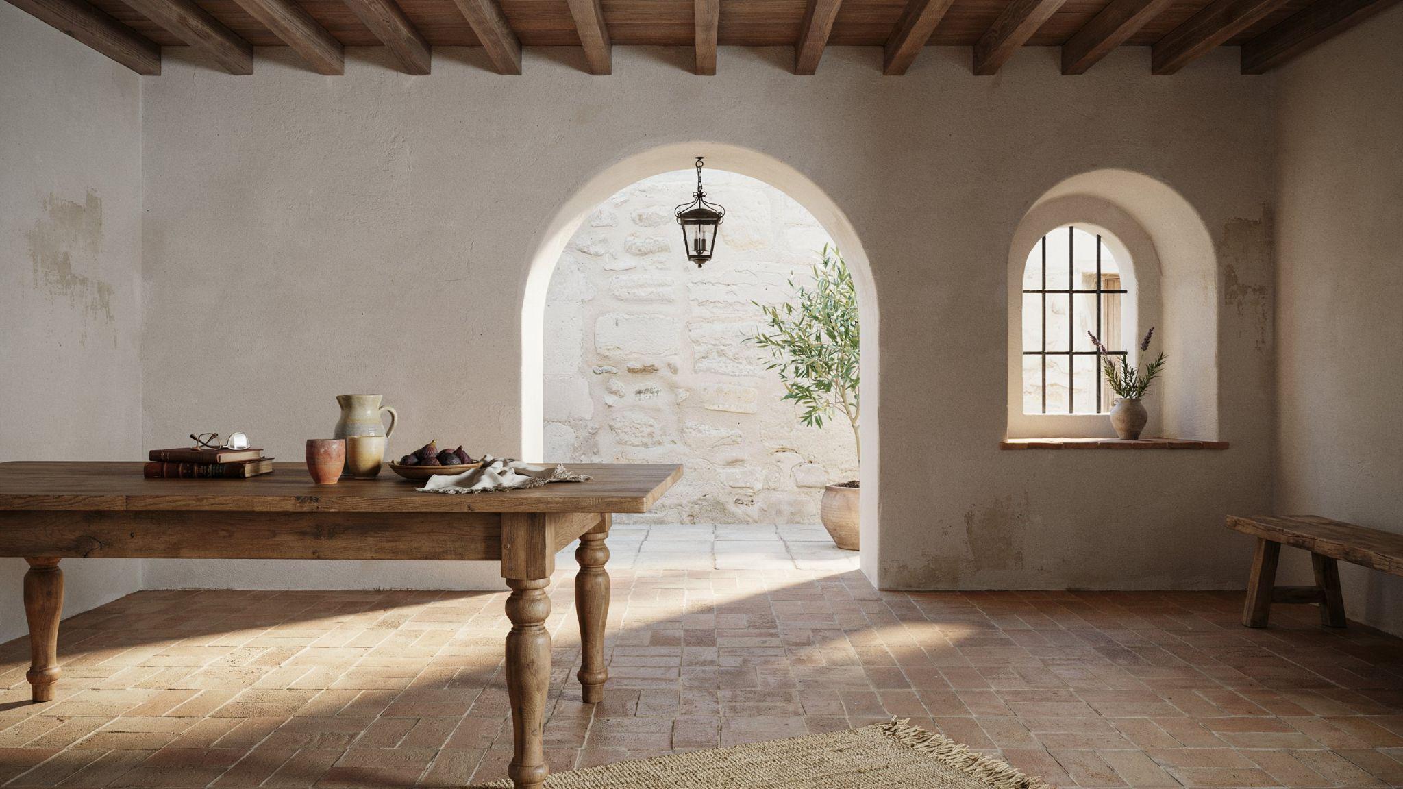 Spanish Mediterranean interior with terracotta tiles, white walls, wood beams, and arched doorways in a warm rustic space.