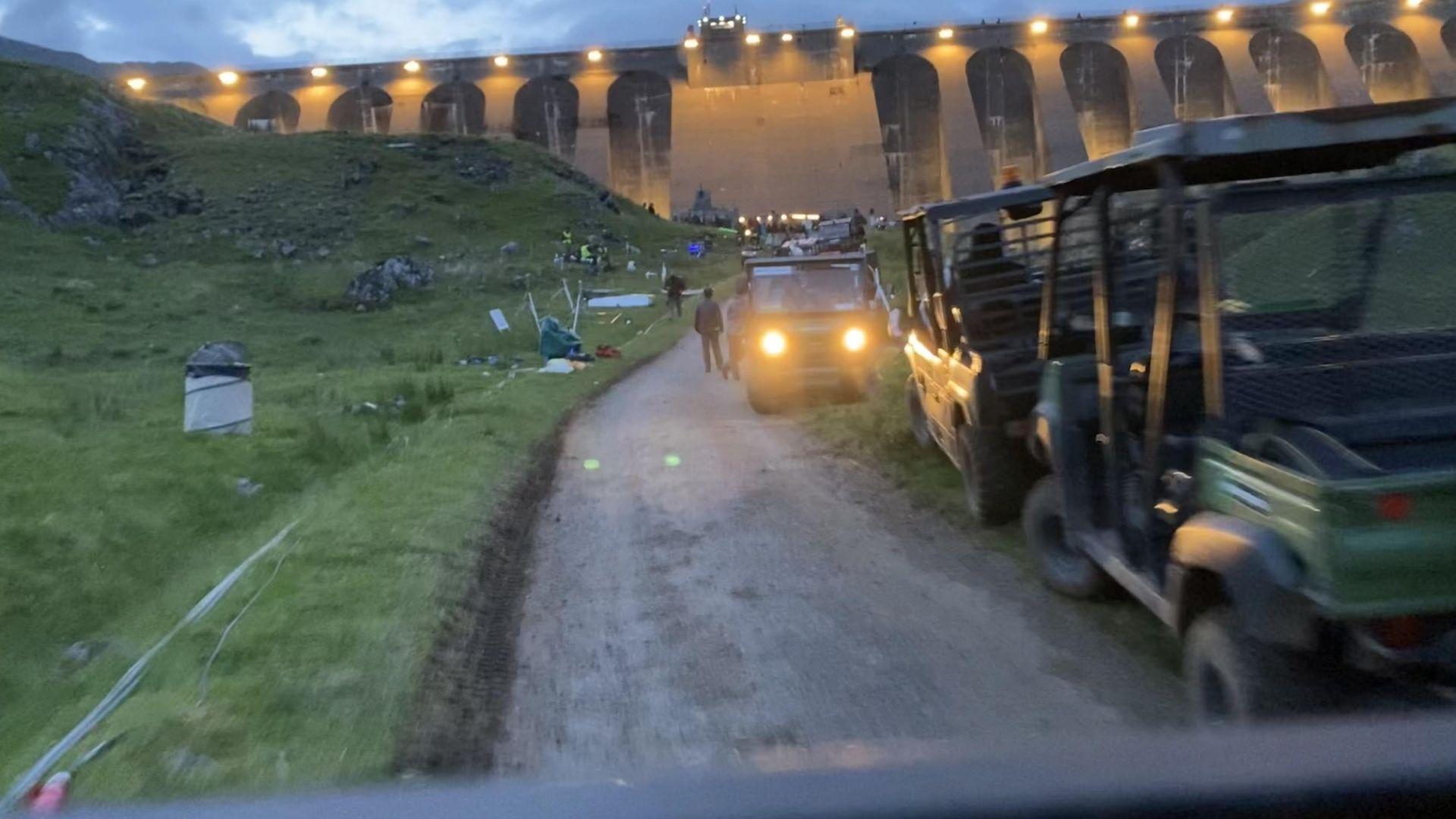 Night shoot at Cruachan Dam, Scotland, with crew vehicles on a gravel path in front of the illuminated arched dam wall.