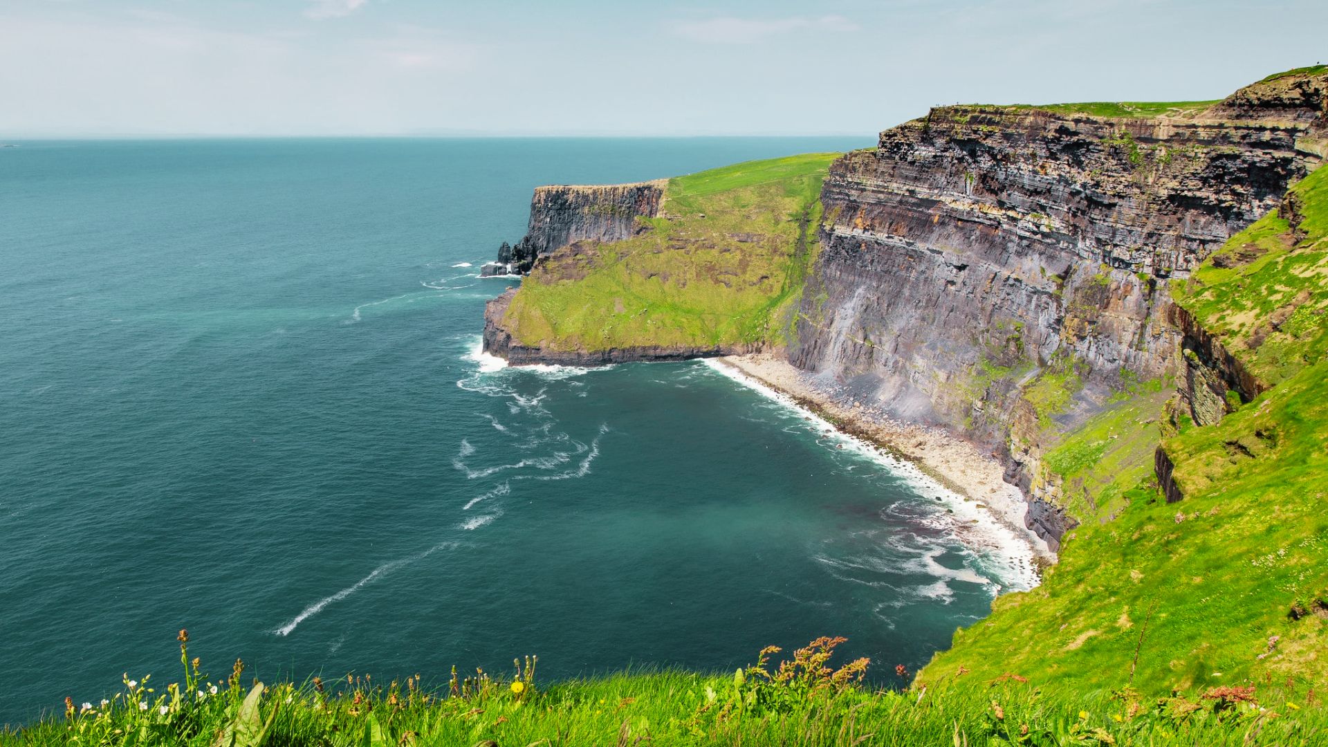 Dramatic sea cliffs plunge into turquoise water along Ireland's Atlantic coast on a clear day.