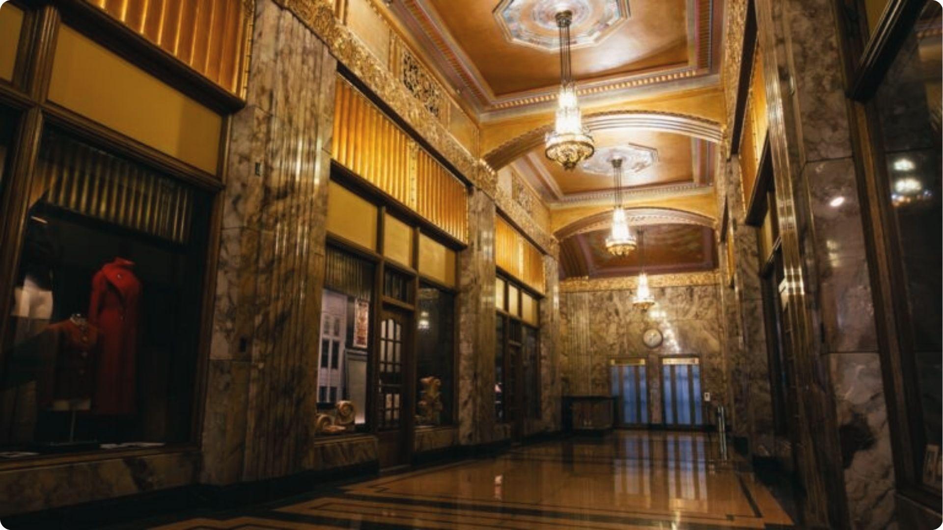 Art Deco marble hallway with chandeliers and red dress display in Tulsa's Philcade Building, used as a Tulsa King filming site.