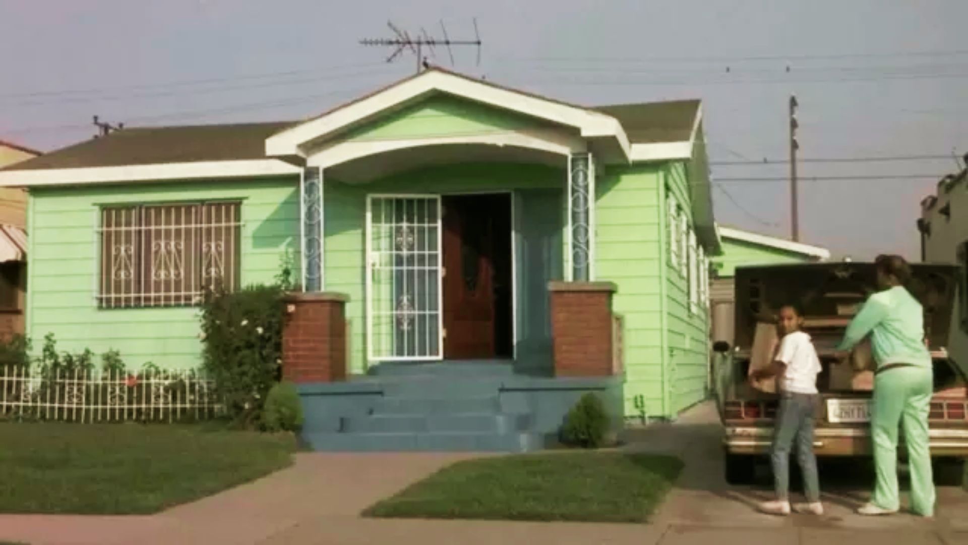 Mint green house number 5914 with white trim, two people unloading a car trunk.