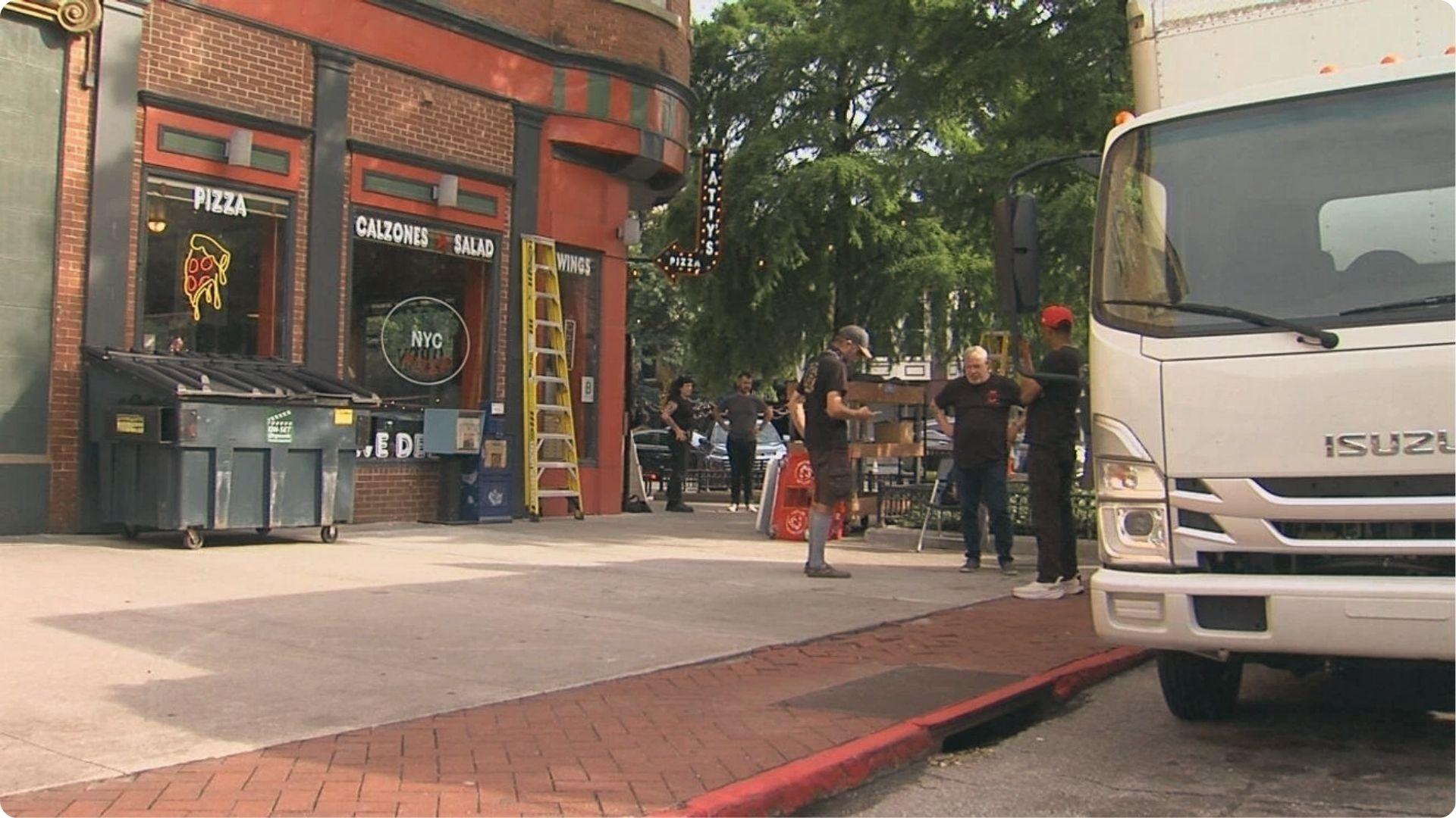 Film crew and Isuzu truck outside Fatty's Pizza with NYC sign in window, a Tulsa location redressed for New York in Tulsa King.