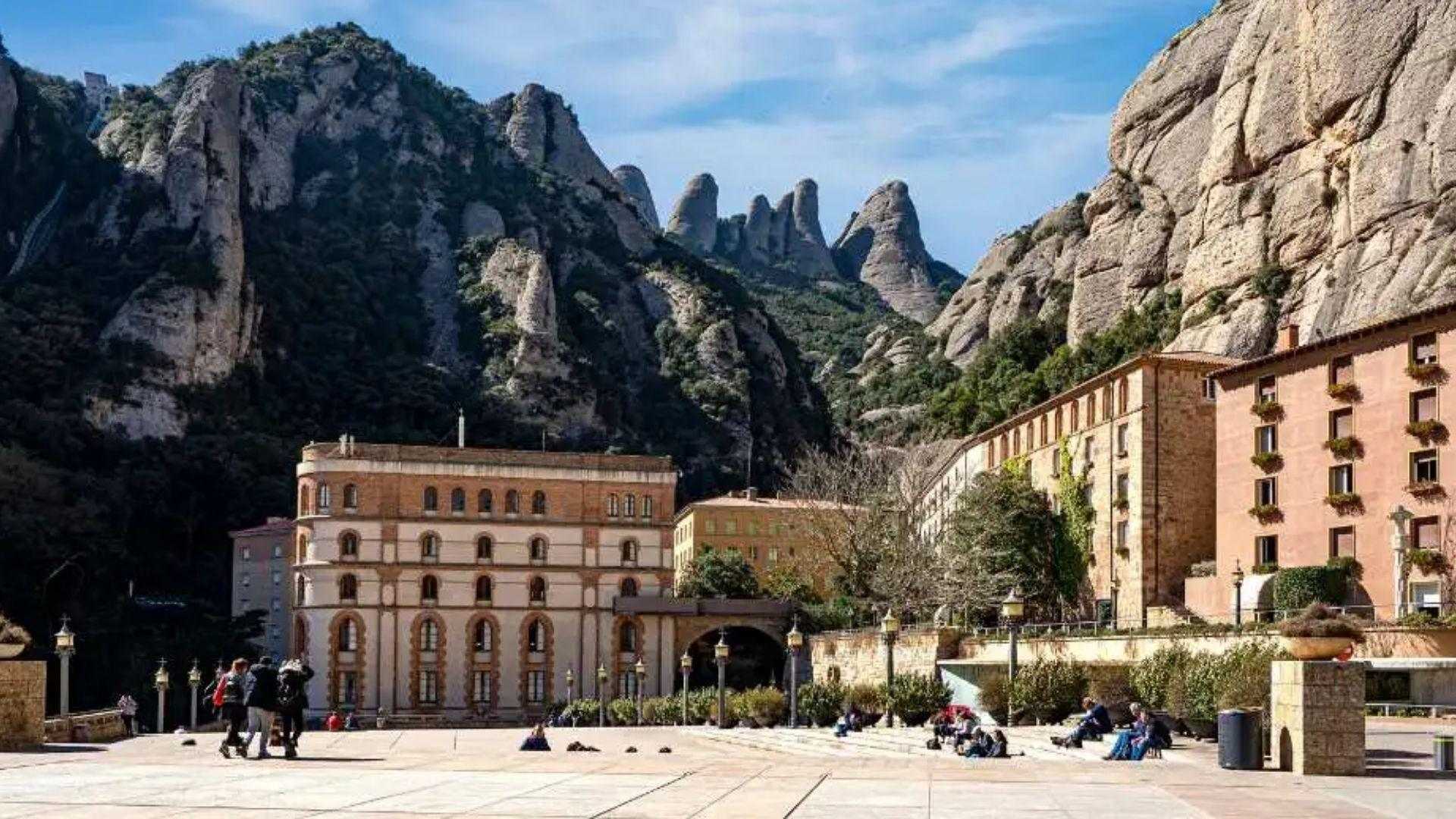 Montserrat Abbey plaza in Catalonia with serrated rock formations behind the monastery buildings.