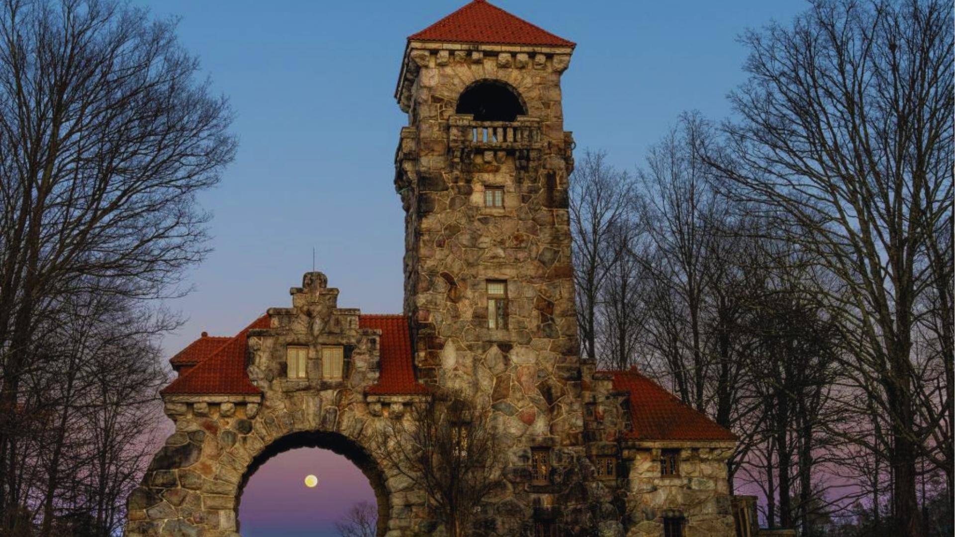 Mohonk Mountain House stone gatehouse tower at dusk with full moon framed in archway, a filming location for exterior shots in Severance Season 1.