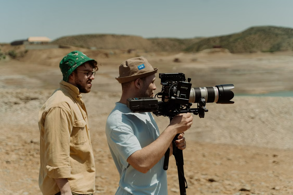 Two filmmakers operating a professional video camera outdoors in a rocky landscape